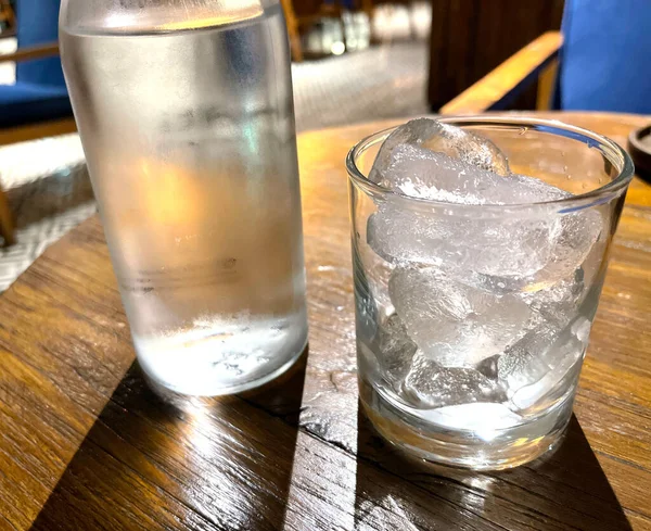 選択的フォーカス 氷とクリアガラスボトルで満たされた透明なガラスは 冷たいミネラルウォーターを木製のテーブルの上に座っている 喉の渇きを癒すための水の使用 — ストック写真