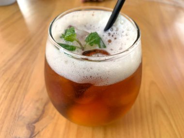 Köpüklü narenciye çayı, narenciyeli organik çay ve ahşap masanın üstünde bir bardak dolusu nane yaprağı.