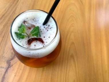 Köpüklü narenciye çayı, narenciyeli organik çay ve ahşap masanın üstünde bir bardak dolusu nane yaprağı.