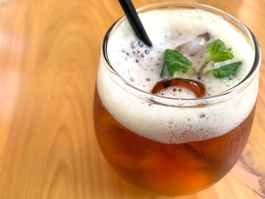 Köpüklü narenciye çayı, narenciyeli organik çay ve ahşap masanın üstünde bir bardak dolusu nane yaprağı.