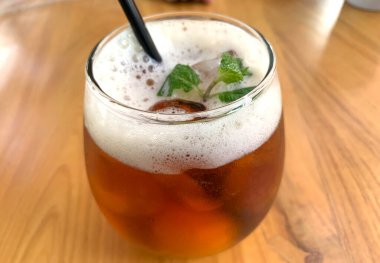 Köpüklü narenciye çayı, narenciyeli organik çay ve ahşap masanın üstünde bir bardak dolusu nane yaprağı.