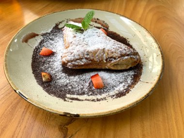 Elma tatlısı, krema şekeri, çilek parçaları ve çikolata sosuyla kaplanmış.