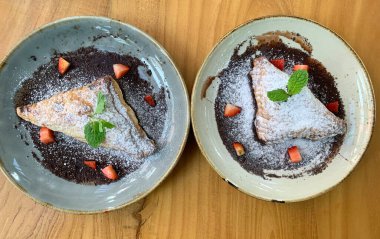 Elma tatlısı, krema şekeri, çilek parçaları ve çikolata sosuyla kaplanmış.