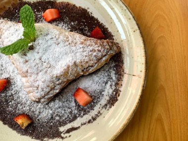 Elma tatlısı, krema şekeri, çilek parçaları ve çikolata sosuyla kaplanmış.