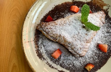 Elma tatlısı, krema şekeri, çilek parçaları ve çikolata sosuyla kaplanmış.