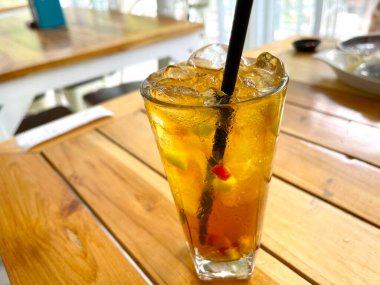 Taze meyve kokteyli alkollü rom ve viskiyle berrak bir bardakta ve ahşap bir masada buz parçasıyla.