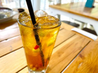 Taze meyve kokteyli alkollü rom ve viskiyle berrak bir bardakta ve ahşap bir masada buz parçasıyla.