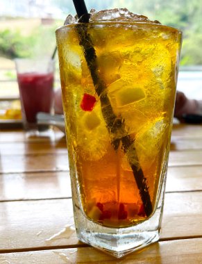 Taze meyve kokteyli alkollü rom ve viskiyle berrak bir bardakta ve ahşap bir masada buz parçasıyla.