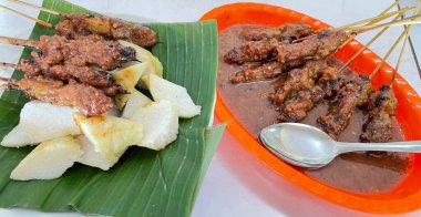 Fıstık sosu ve muz yaprağında pirinç keki ile servis edilen kömürün üzerinde ızgara yapılmış çok lezzetli sığır eti satay eti.