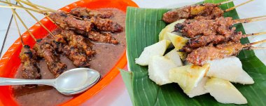 Fıstık sosu ve muz yaprağında pirinç keki ile servis edilen kömürün üzerinde ızgara yapılmış çok lezzetli sığır eti satay eti.