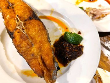 Lezzetli kızarmış İspanyol uskumru balığı baharatlı sos ve turunçgiller bir restoranda beyaz tabakta servis ediliyor.