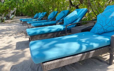 Lüks tropikal otel ya da tatil köylerinde sıcak yaz gününde beyaz kumsalda şezlonglar ya da plaj sandalyeleri. Seyahat, turizm, tatil, tatil konsepti. Palmiye ağaçları, yeşillik