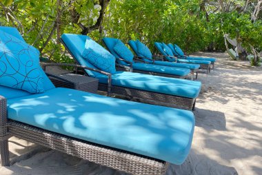 Lüks tropikal otel ya da tatil köylerinde sıcak yaz gününde beyaz kumsalda şezlonglar ya da plaj sandalyeleri. Seyahat, turizm, tatil, tatil konsepti. Palmiye ağaçları, yeşillik