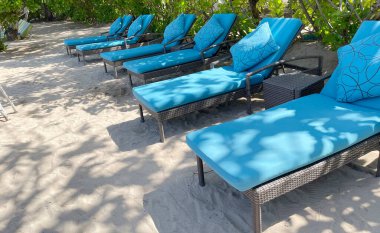 Lüks tropikal otel ya da tatil köylerinde sıcak yaz gününde beyaz kumsalda şezlonglar ya da plaj sandalyeleri. Seyahat, turizm, tatil, tatil konsepti. Palmiye ağaçları, yeşillik