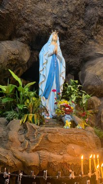 Kutsal Bakire Meryem Anıtı Roma Katolik Kilisesi 'nde, Bakire Meryem Mağarasında, bir kaya mağarası Katolik Kilisesi' nde, etrafında tropikal çiçekler olan Asyalı bir kilisede.