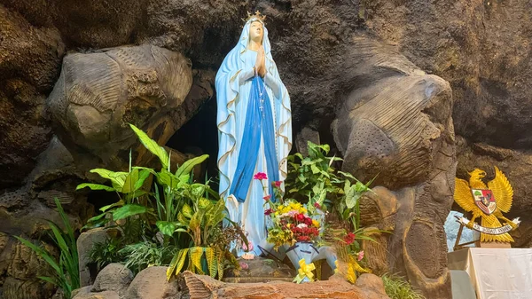 Kutsal Bakire Meryem Anıtı Roma Katolik Kilisesi 'nde, Bakire Meryem Mağarasında, bir kaya mağarası Katolik Kilisesi' nde, etrafında tropikal çiçekler olan Asyalı bir kilisede.