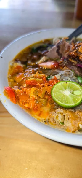 Indonesian style beef noodle soup called soto mie, freshly made soup with vermicelli rice noodle, fried shallots, chilli paste, and fried rissoles and fresh lime juice