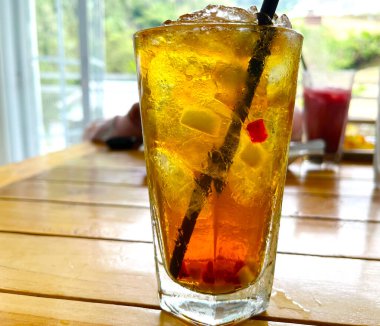 Taze meyve kokteyli alkollü rom ve viskiyle berrak bir bardakta ve ahşap bir masada buz parçasıyla.