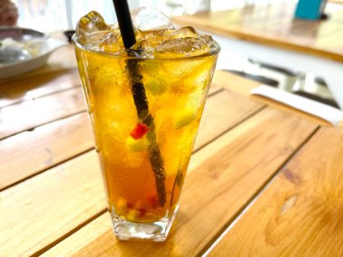 Taze meyve kokteyli alkollü rom ve viskiyle berrak bir bardakta ve ahşap bir masada buz parçasıyla.