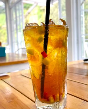 Taze meyve kokteyli alkollü rom ve viskiyle berrak bir bardakta ve ahşap bir masada buz parçasıyla.