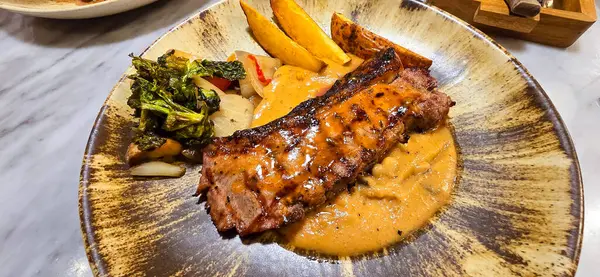 New york strip loin beef steak meat with mushroom sauce and potato wedges and salad plated on beautiful plate on a steak house