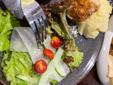 Tavuk cordon bleu tabağı, kızarmış tavuk göğsü peynirle doldurulmuş ve kremayla eritilmiş salata ve patates püresi kahverengi tabakta servis ediliyor.