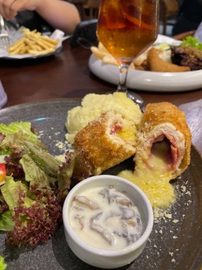 Tavuk cordon bleu tabağı, kızarmış tavuk göğsü peynirle doldurulmuş ve kremayla eritilmiş salata ve patates püresi kahverengi tabakta servis ediliyor.