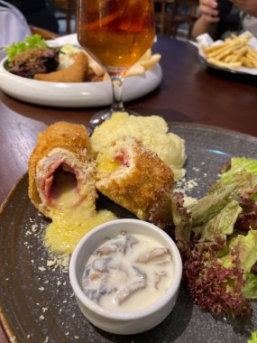 Tavuk cordon bleu tabağı, kızarmış tavuk göğsü peynirle doldurulmuş ve kremayla eritilmiş salata ve patates püresi kahverengi tabakta servis ediliyor.