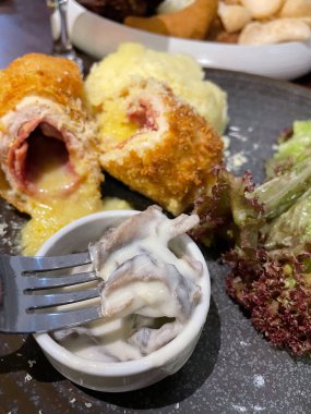 Tavuk cordon bleu tabağı, kızarmış tavuk göğsü peynirle doldurulmuş ve kremayla eritilmiş salata ve patates püresi kahverengi tabakta servis ediliyor.