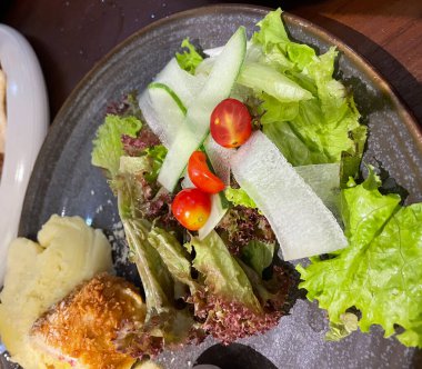 Tavuk cordon bleu tabağı, kızarmış tavuk göğsü peynirle doldurulmuş ve kremayla eritilmiş salata ve patates püresi kahverengi tabakta servis ediliyor.