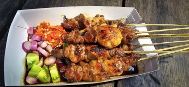 Izgara satay, barbekü sosu ve soğan, acı biber ve salatalık turşusu ile servis edilir. Ahşap masanın üstünde seçici odak fotoğrafı.
