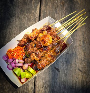 Lamb grilled satay served with barbecue savory sauce and pickled onion, chili and cucumber, selective focus photo on top of wooden table clipart