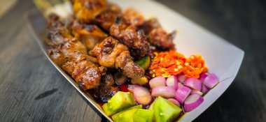 Lamb grilled satay served with barbecue savory sauce and pickled onion, chili and cucumber, selective focus photo on top of wooden table clipart
