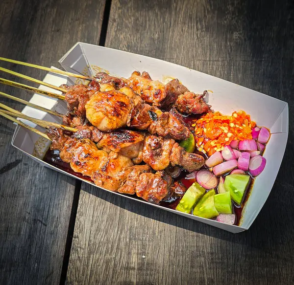 stock image Lamb grilled satay served with barbecue savory sauce and pickled onion, chili and cucumber, selective focus photo on top of wooden table