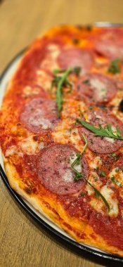 Eritilmiş mozarella peynirli taze pişmiş New York usulü pizza ve masadaki ahşap tahtaya yakın plan domates sosu. Bol pepperonili.