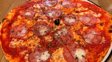 Eritilmiş mozarella peynirli taze pişmiş New York usulü pizza ve masadaki ahşap tahtaya yakın plan domates sosu. Bol pepperonili.