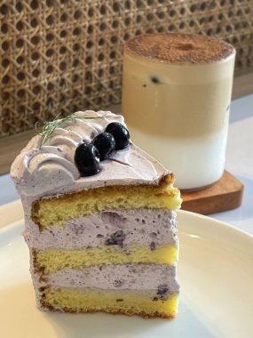 Beyaz tabakta taze böğürtlenlerle süslenmiş bir dilim yaban mersinli kek, lezzetli katmanlı pasta, kafenin üst manzarası.