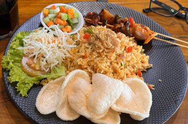 Ateşli pilav ya da Nasi Goreng Endonezya tavuğu salatalık turşusu ve soğan ile servis edilen kızarmış pilav ve satay soslu karides krakeri.