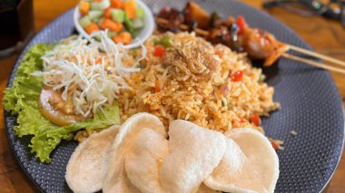 Ateşli pilav ya da Nasi Goreng Endonezya tavuğu salatalık turşusu ve soğan ile servis edilen kızarmış pilav ve satay soslu karides krakeri.