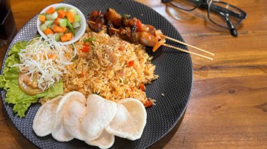Ateşli pilav ya da Nasi Goreng Endonezya tavuğu salatalık turşusu ve soğan ile servis edilen kızarmış pilav ve satay soslu karides krakeri.
