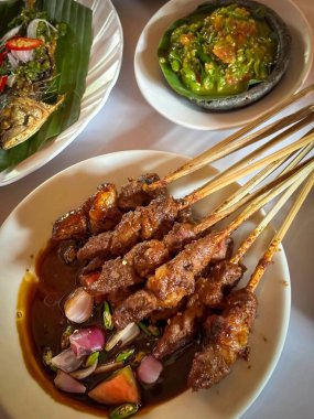 Kuzu eti, ızgara şiş. Soya soslu, soğanlı, domatesli, salatalıklı ve kırmızı biberli, beyaz tabakta servis edilmiş.