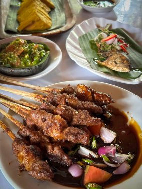 Kuzu eti, ızgara şiş. Soya soslu, soğanlı, domatesli, salatalıklı ve kırmızı biberli, beyaz tabakta servis edilmiş.