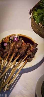 Kuzu eti, ızgara şiş. Soya soslu, soğanlı, domatesli, salatalıklı ve kırmızı biberli, beyaz tabakta servis edilmiş.