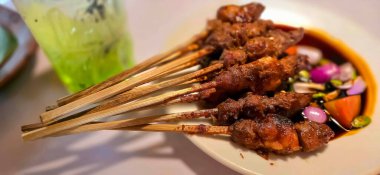Kuzu eti, ızgara şiş. Soya soslu, soğanlı, domatesli, salatalıklı ve kırmızı biberli, beyaz tabakta servis edilmiş.