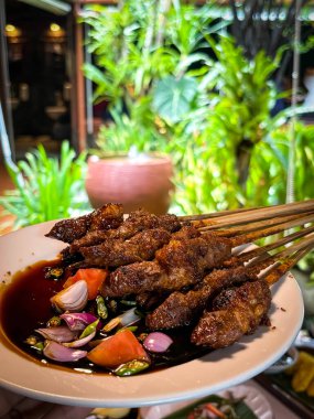 Kuzu eti, ızgara şiş. Soya soslu, soğanlı, domatesli, salatalıklı ve kırmızı biberli, beyaz tabakta servis edilmiş.