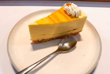 Limonlu cheesecake taze pişmiş dilim, New York usulü klasik peynirli kek tatlı tabağında. Tatlı kaşığıyla servis edilen beyaz tabakta bir dilim lezzetli pasta, yemek kitabına iyi gelir.