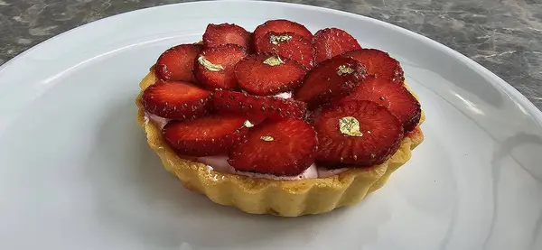 stock image Delicious strawberry tart or tartlet with cut out strawberries and whipped cream decorated with edible gold flakes, good for multimedia recipe content creation