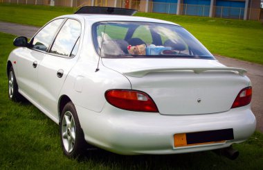 Çimenli bir alana park etmiş, şık tasarımı ve işlevselliği açık havada sergilenen şık beyaz sedan, araba yemyeşil ortamda göze çarpıyor.