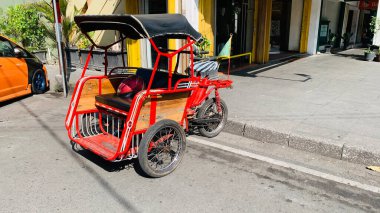 pedicab or rickshaw or locals calls it becak with a canopy is parked on a sunny street, reflecting a vibrant urban scene. The vehicle features a padded seat and unique design, typical in Southeast Asia. clipart