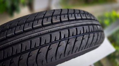 Gıcır gıcır yeni bir araba lastiğinin detaylı görüntüsü. Gelişmiş tutuş ve performans için karmaşık lastik kalıplarını gösteriyor.